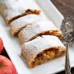 This delectable Apple Strudel recipe is a classic German pastry filled with crisp apples, golden raisins, almonds, and that sweet taste of cinnamon and sugar. It's the perfect dessert for Fall and the approaching Holiday Season!