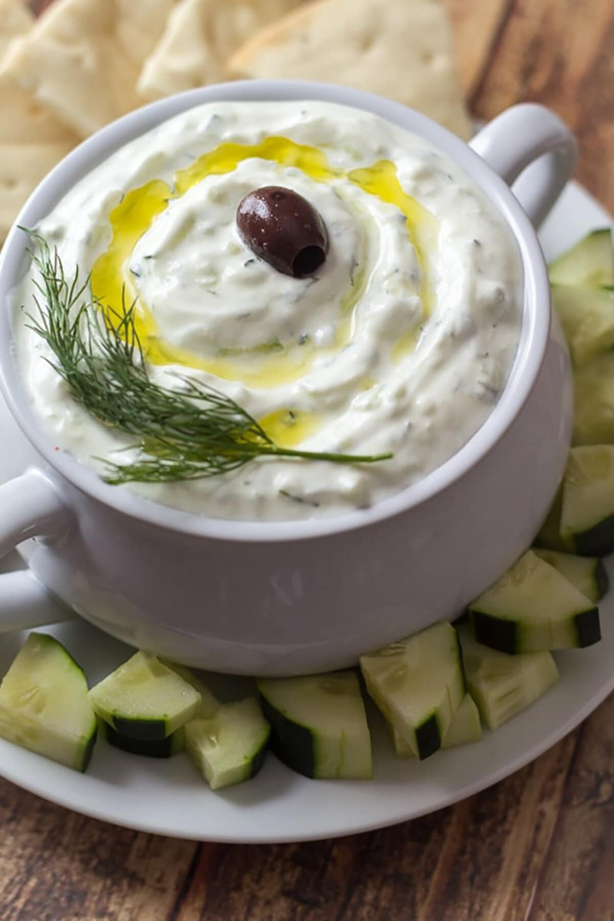 Authentic tzatziki in white bowl with chopped cucumbers and pita bread around it.