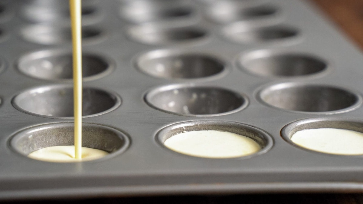 Batter being poured into a mini muffin tin.