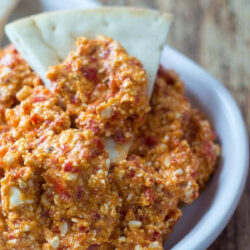 Greek red pepper feta dip on a platter and on a pita triangle.