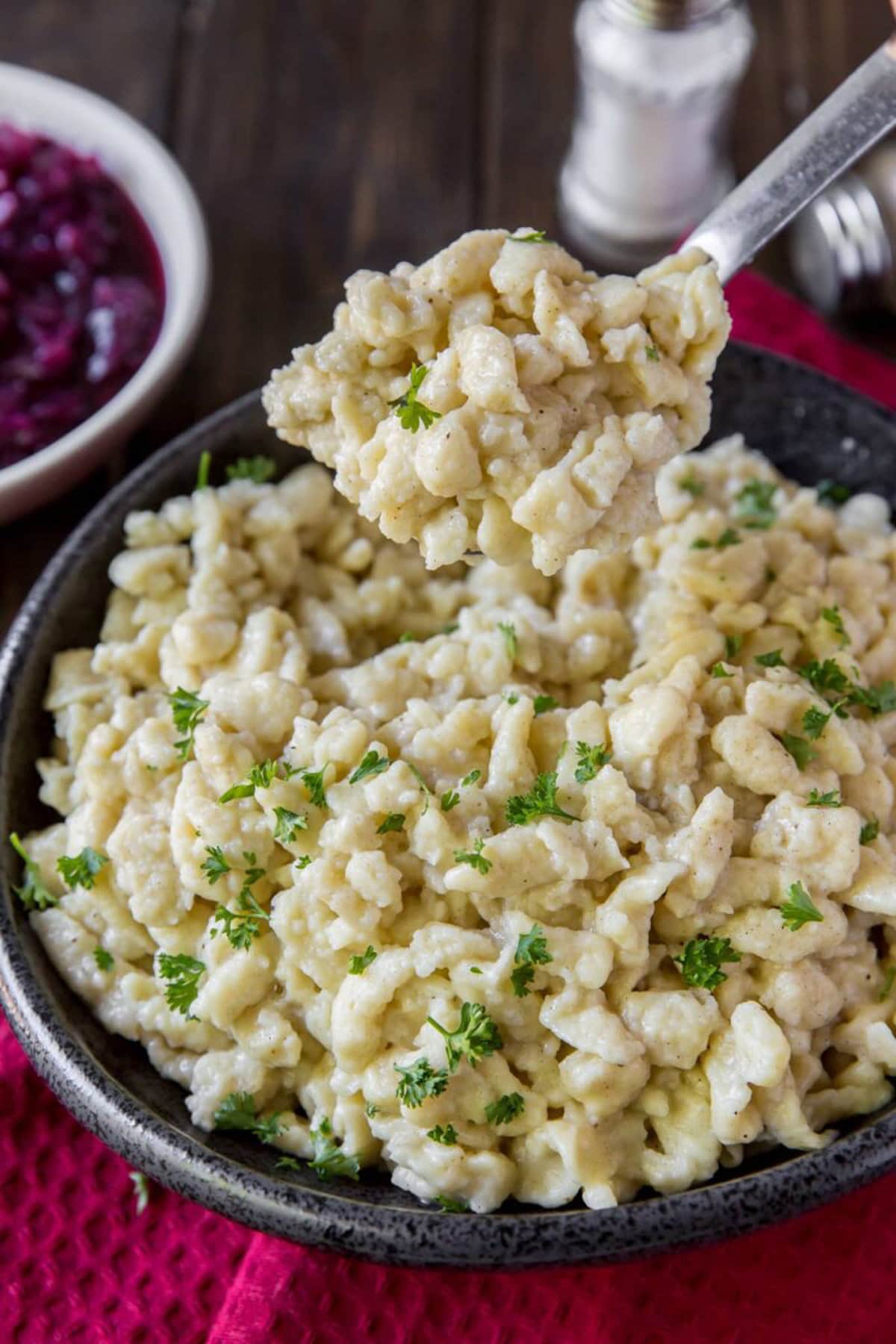 German Spaetzle in a serving dish with red cabbage in a white bowl.
