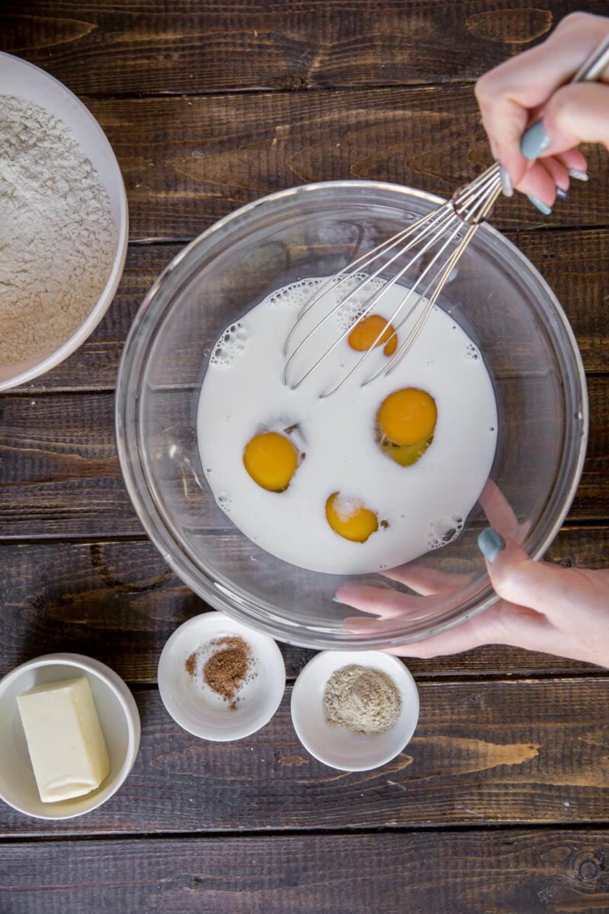 Milk, eggs and salt being mixed in a clear bowl.