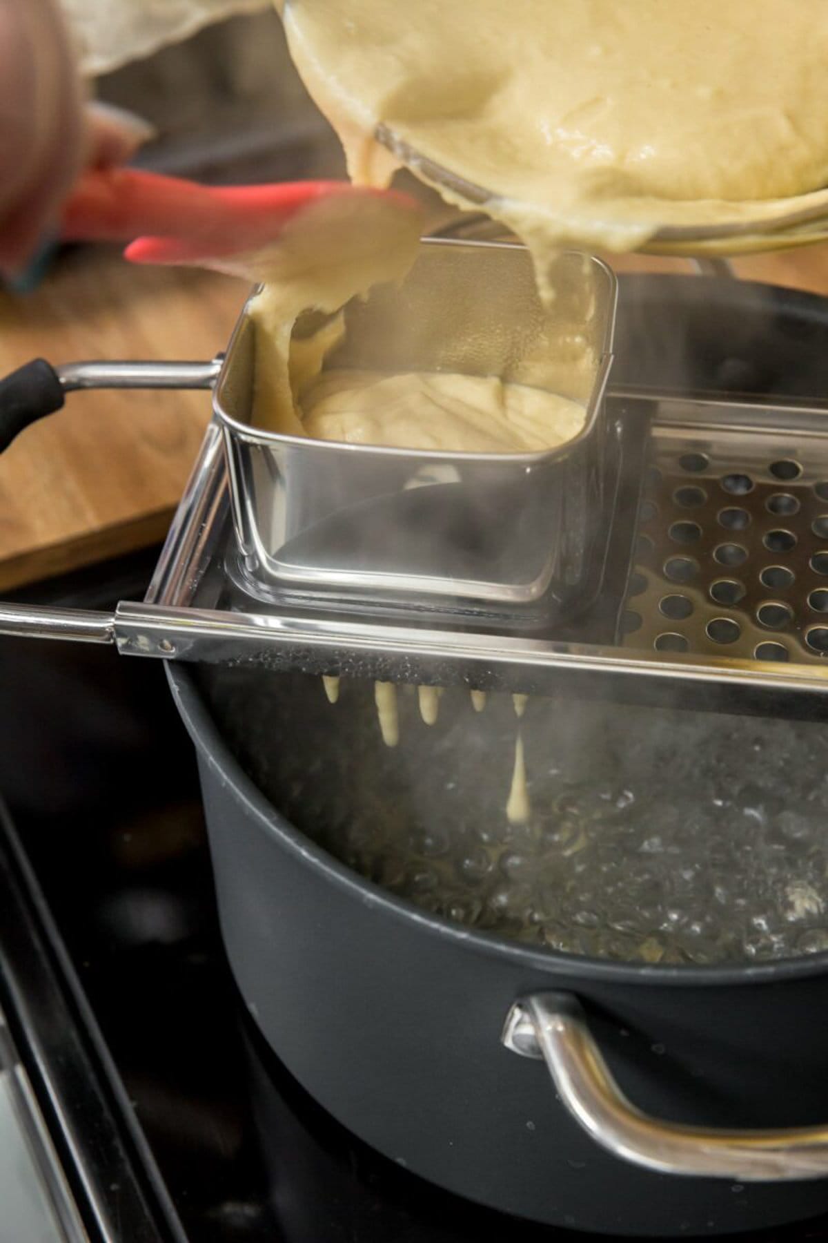 Spaetzle batter poured into a spaetzle maker over a pot of boiling water.