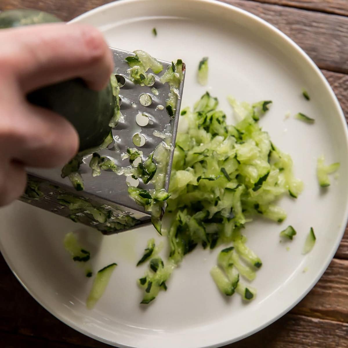 grating cucumber over a white plate