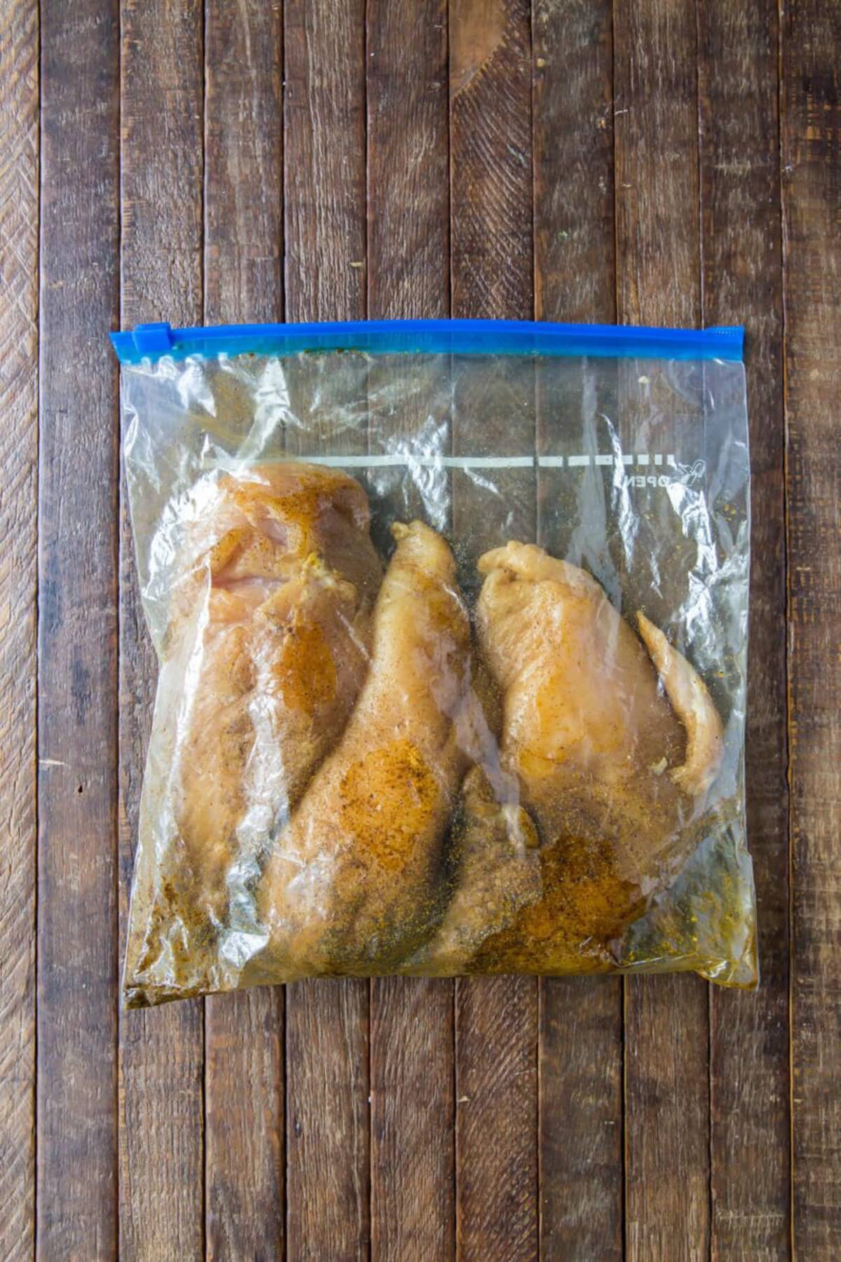 Chicken marinating in a bag on a table.