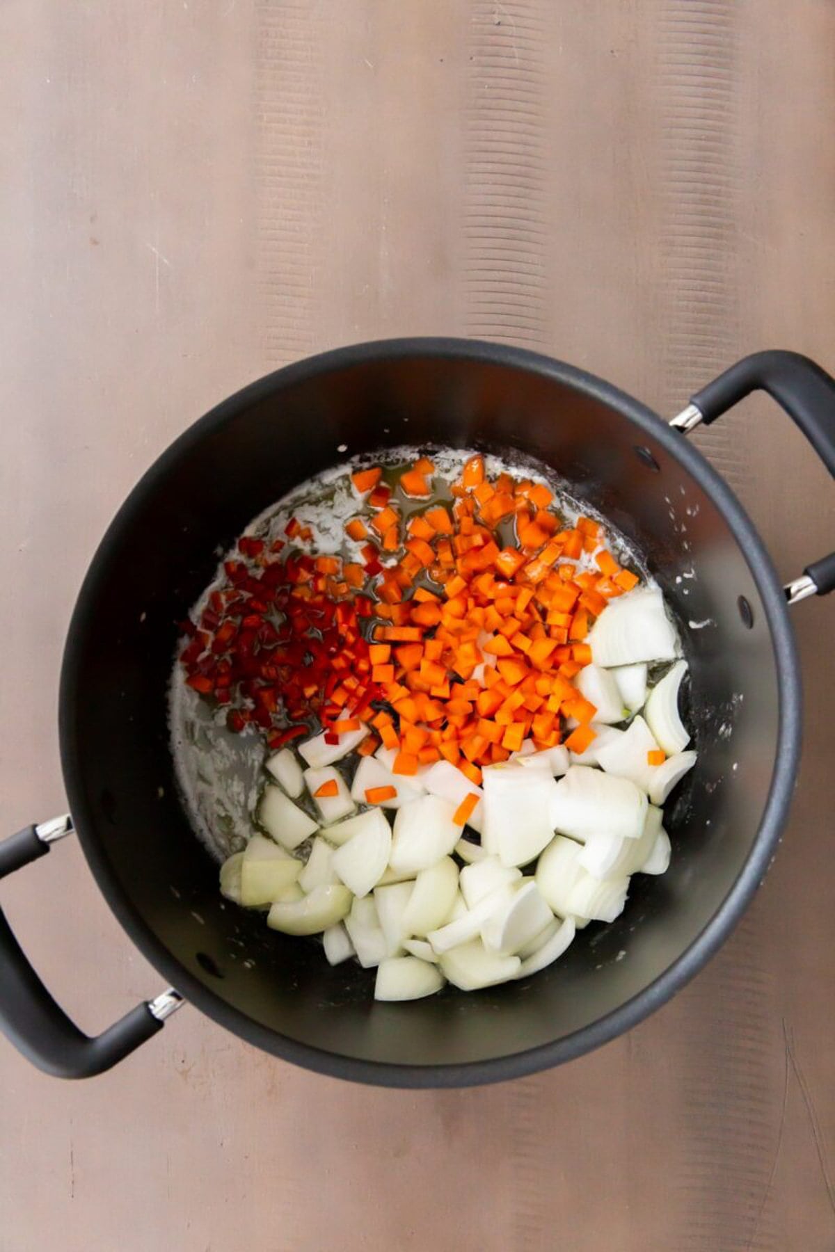 Onions, carrots, and peppers cooking in a pot.