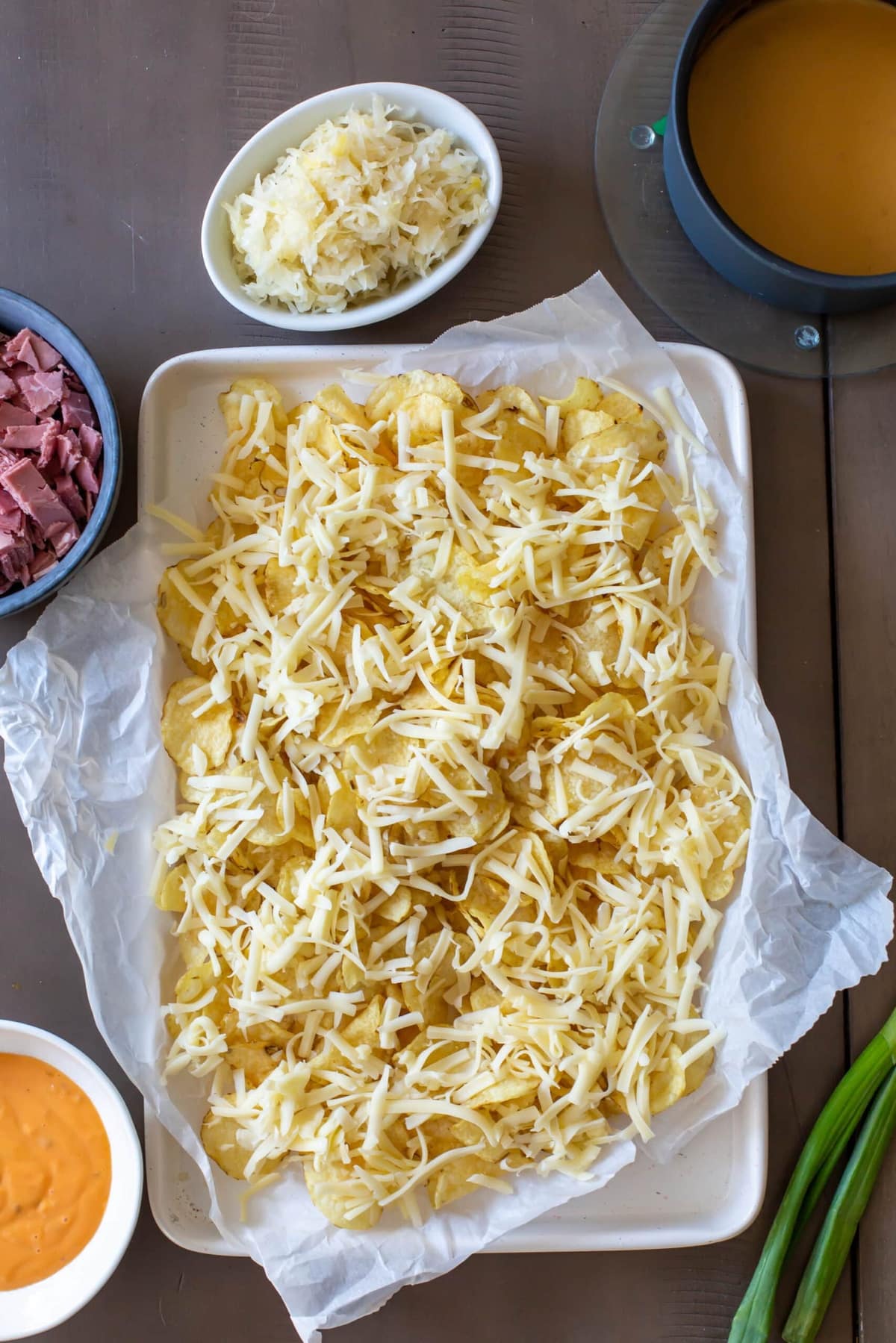 A plate of potato chips is topped with cheese and placed on the rim of a baking sheet.
