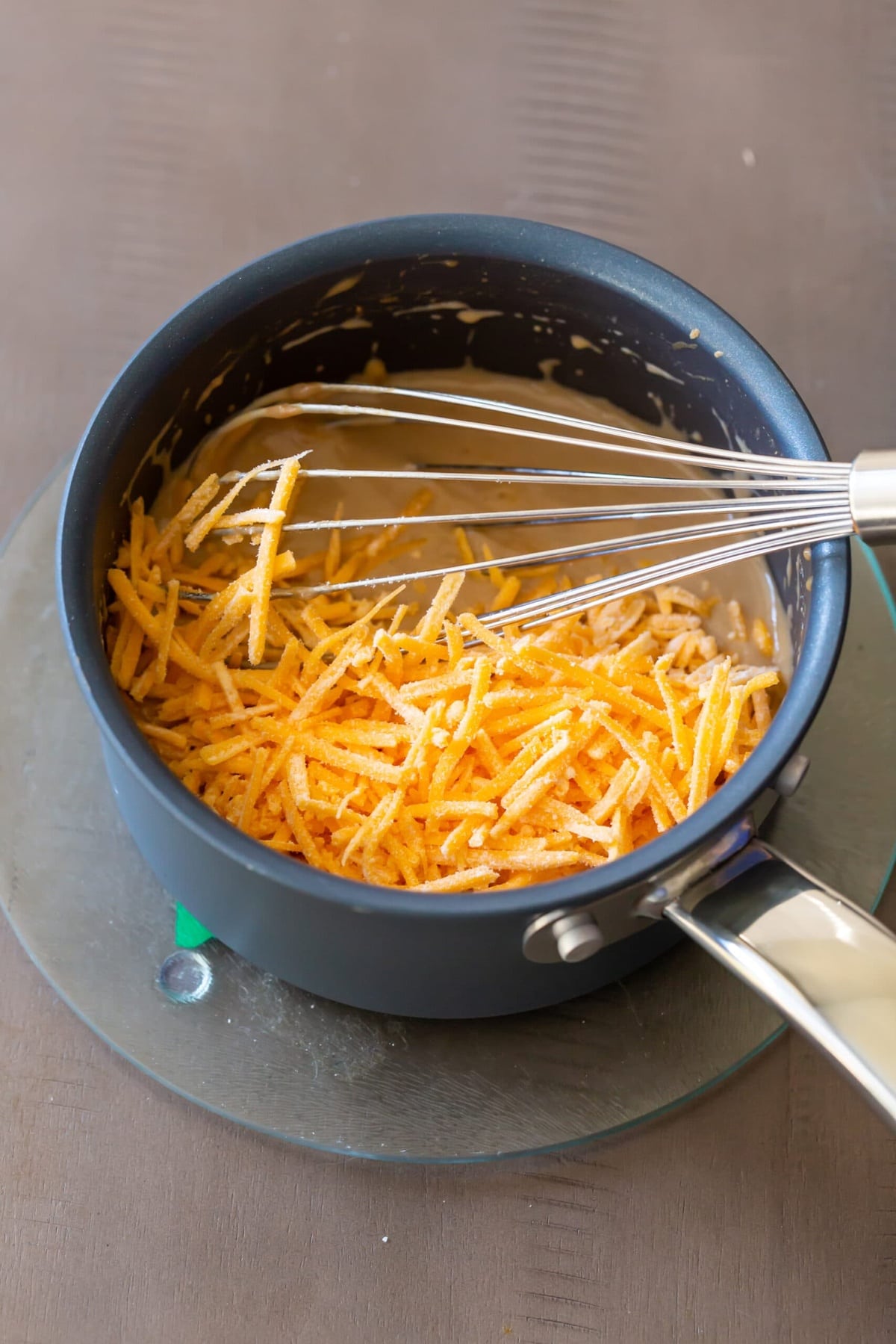 Adding grated cheddar cheese and constantly stirring it into the mixture.




