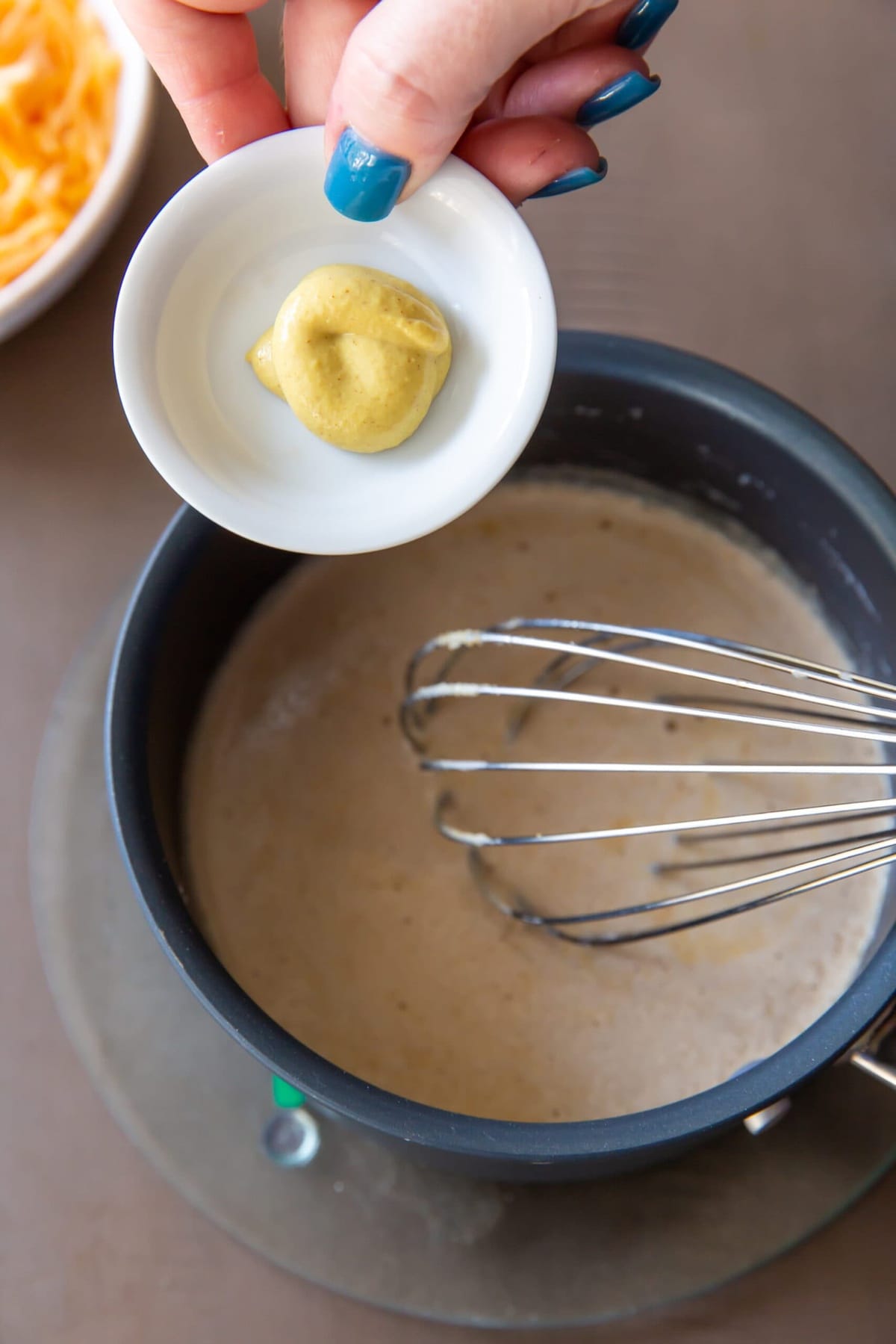 Adding Dijon mustard to the mixture while maintaining a continuous whisking motion to make sure it's evenly blended.




