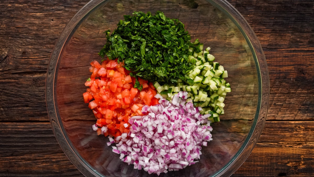 Vegetables and fresh herbs diced up in a glass bowl.
