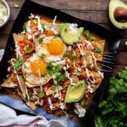 This delicious Mexican Chilaquiles Rojos recipe has triangles of corn tortillas simmered in salsa, and served with cheese, shredded chicken, eggs or beans.