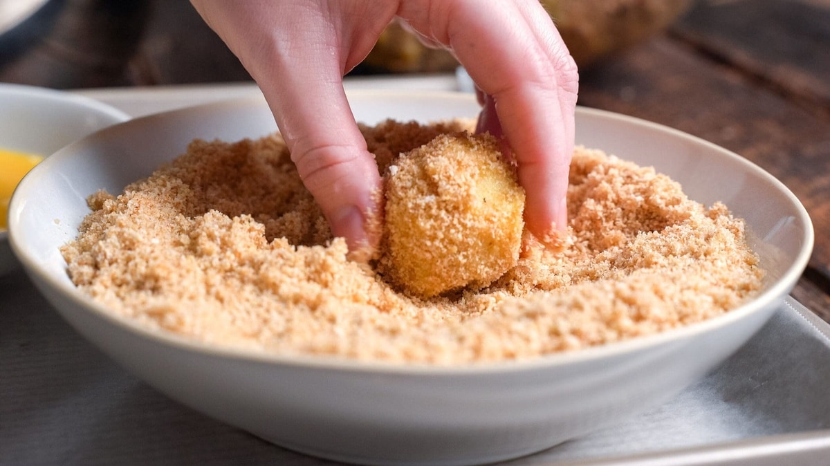 Potato balls being rolled in breadcrumbs.