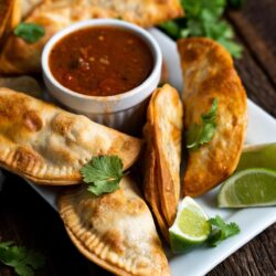Puerto Rican Empanadas on a white plate with a bowl of salsa