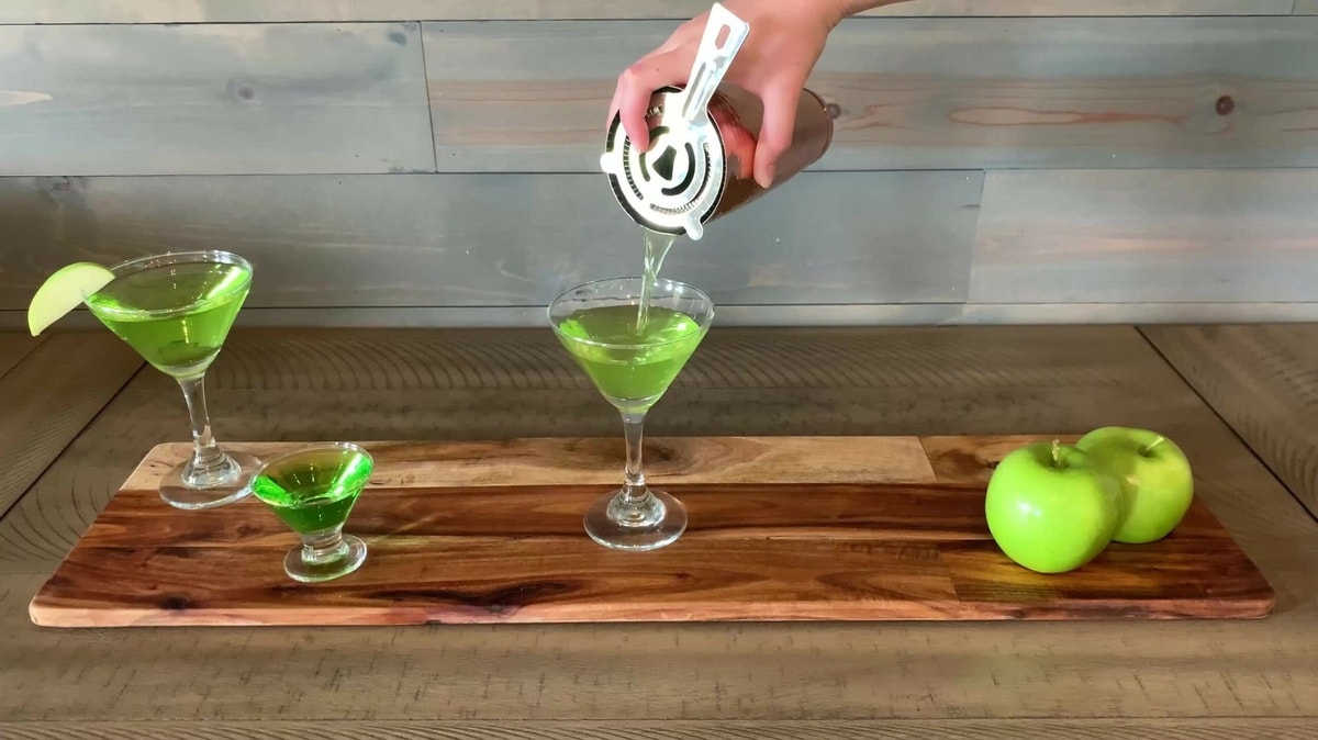 A mixed drink is being poured into a martini glass.