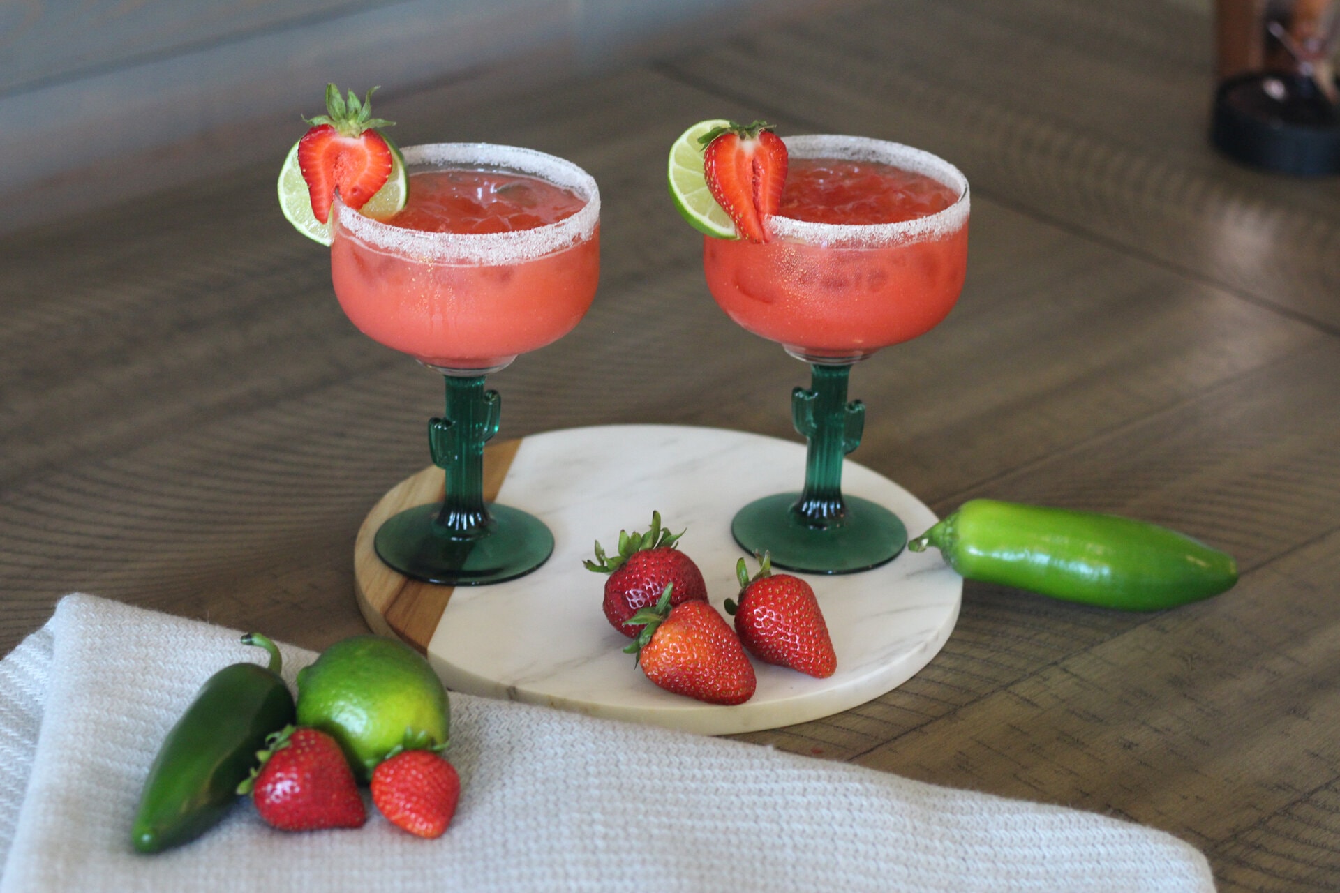Margaritas sitting on a marble board with strawberries and jalapenos around