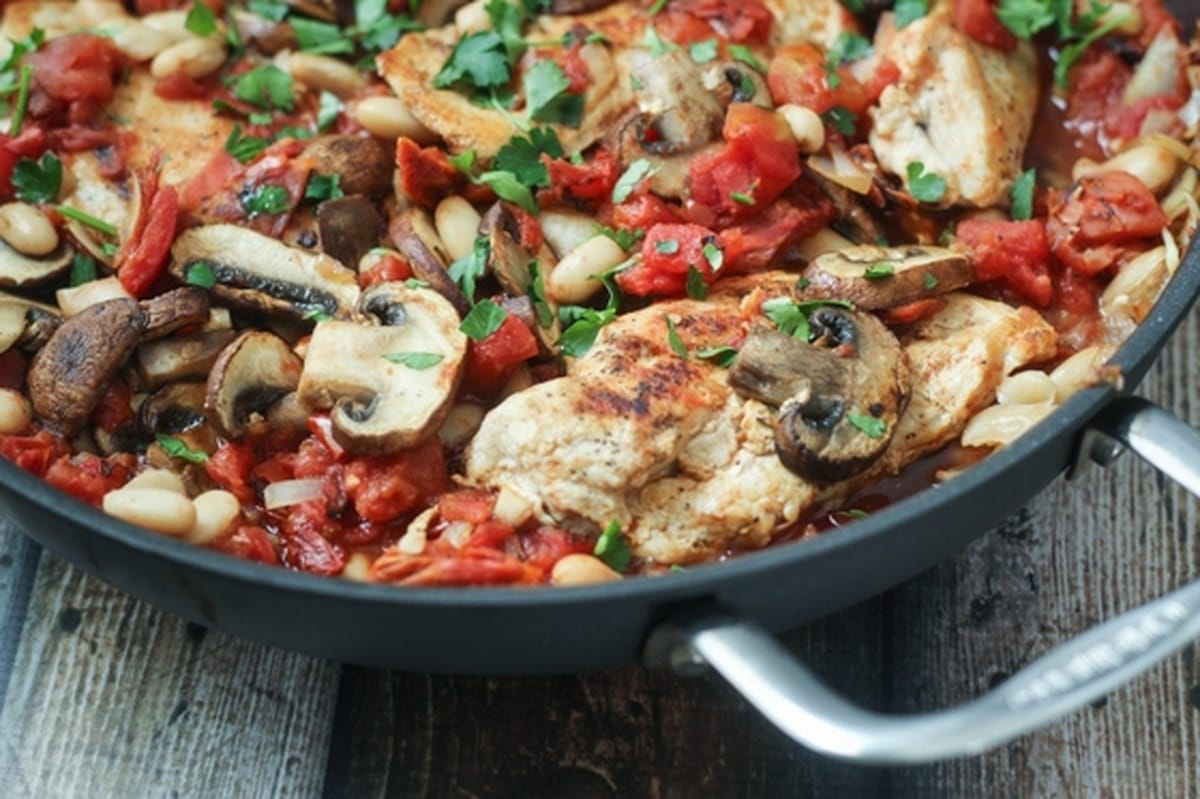 Tuscan chicken in a skillet with mushrooms on top, garnished with parsley.